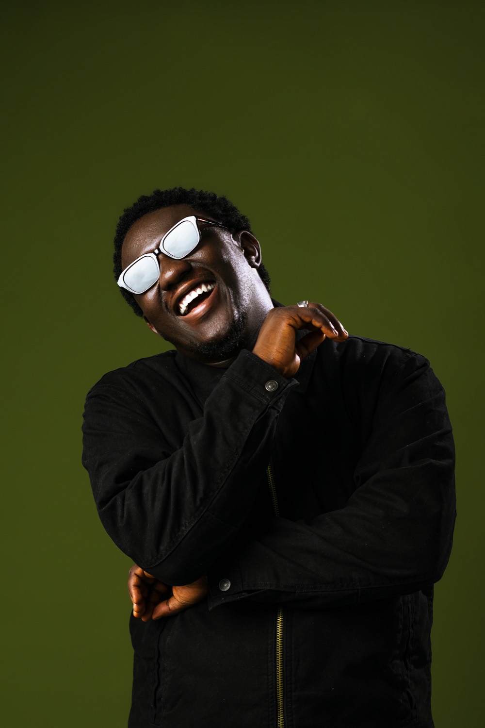 Salem King laughing in a black jacket against an olive backdrop